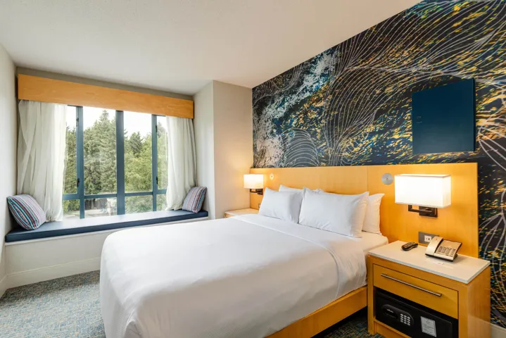 Bedroom featuring a window seat with cushions, a decorative accent wall, a light wood headboard, and integrated bedside lighting