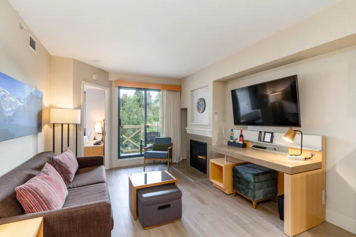 Living area featuring wood-finish flooring, a built-in electric fireplace, a wall-mounted television, and a dedicated desk space with integrated lighting