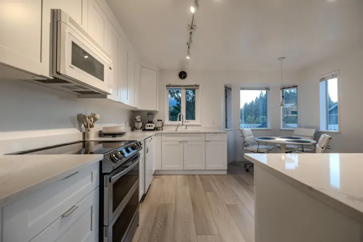 Kitchen featuring white appliances, light wood-style floors, white cabinetry, light stone counters, and pendant lighting