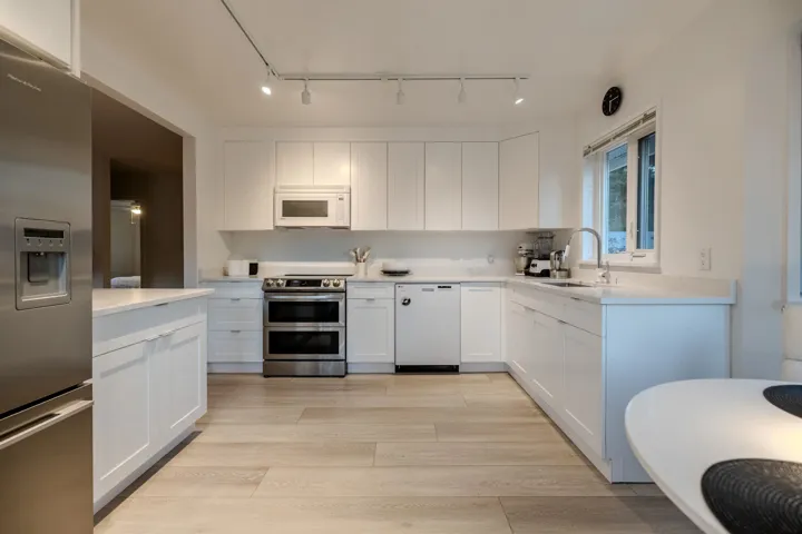 Kitchen with white cabinetry, appliances with stainless steel finishes, light wood-type flooring, and light stone counters