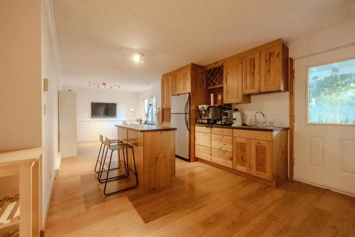 Kitchen featuring a kitchen island, light wood-type flooring, freestanding refrigerator, a kitchen bar, and dark countertops