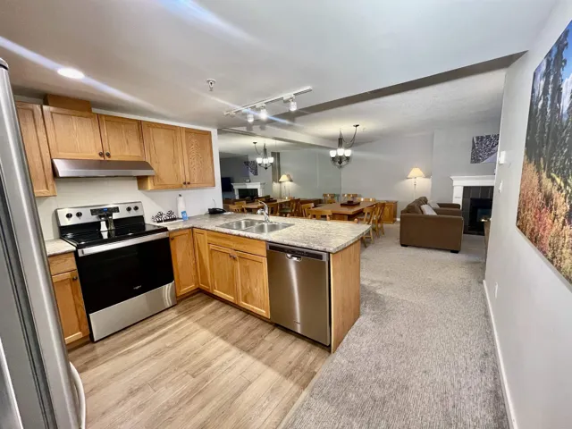 Kitchen featuring open floor plan, under cabinet range hood, appliances with stainless steel finishes, a tile fireplace, and a sink