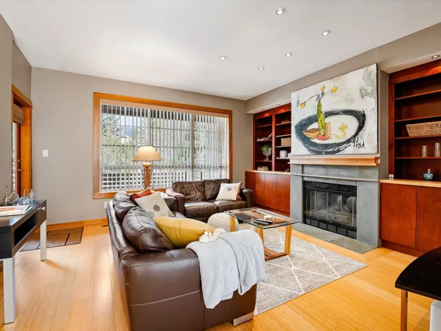 Living room featuring built in shelves, a fireplace with flush hearth, wood finished floors, baseboards, and recessed lighting