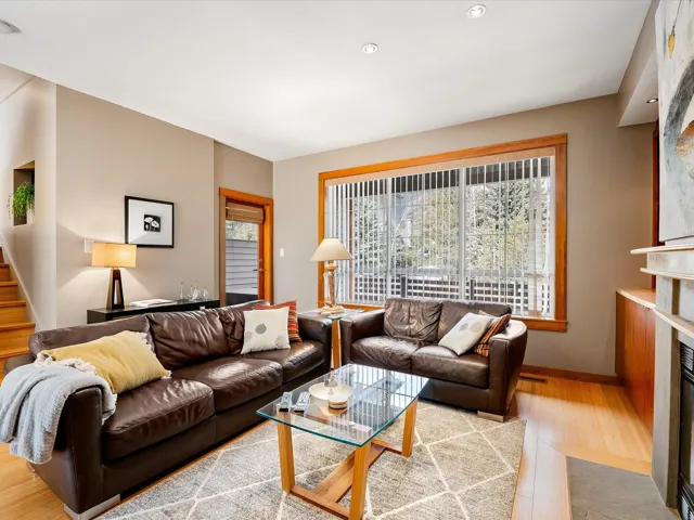 Living room featuring a fireplace with flush hearth, visible vents, baseboards, wood finished floors, and stairway