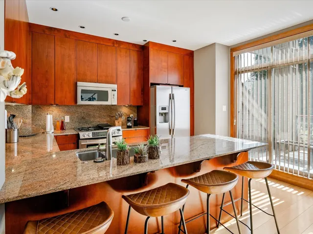 Kitchen featuring a peninsula, decorative backsplash, brown cabinets, fridge with ice dispenser, and white microwave