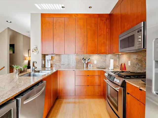 Kitchen with decorative backsplash, a sink, light stone counters, and appliances with stainless steel finishes