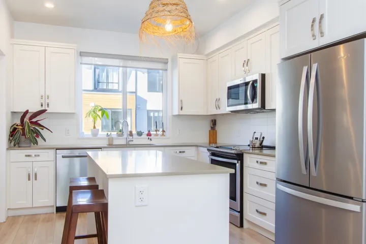 Kitchen featuring appliances with stainless steel finishes, decorative backsplash, a sink, and white cabinets
