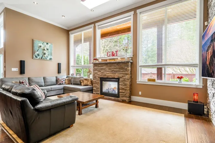 Living room featuring a stone fireplace, hardwood / wood-style floors, ornamental molding, and a skylight