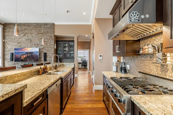 Kitchen featuring dark wood finish cabinetry, stainless steel appliances, dark wood-type flooring, ornamental molding, and light stone countertops