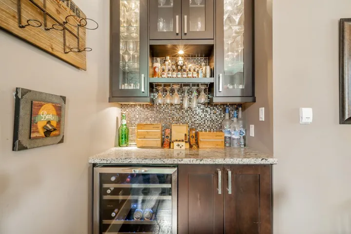 Indoor dry bar featuring glass insert cabinets, light stone countertops, and beverage cooler