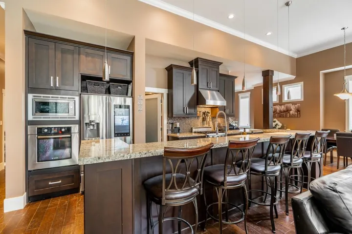 Kitchen with light stone countertops, stainless steel appliances, dark wood finish cabinets, and crown molding