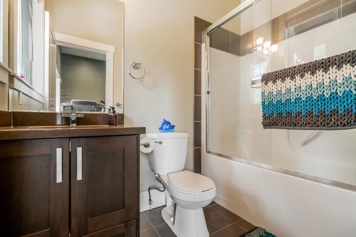 Full bathroom with enclosed tub / shower combo, vanity, dark tile patterned flooring, and a chandelier