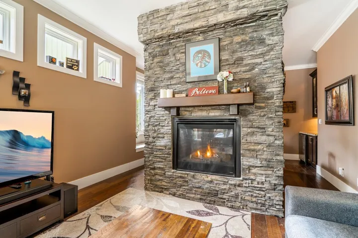 Living room featuring crown molding, dark wood finished floors, and a stone fireplace