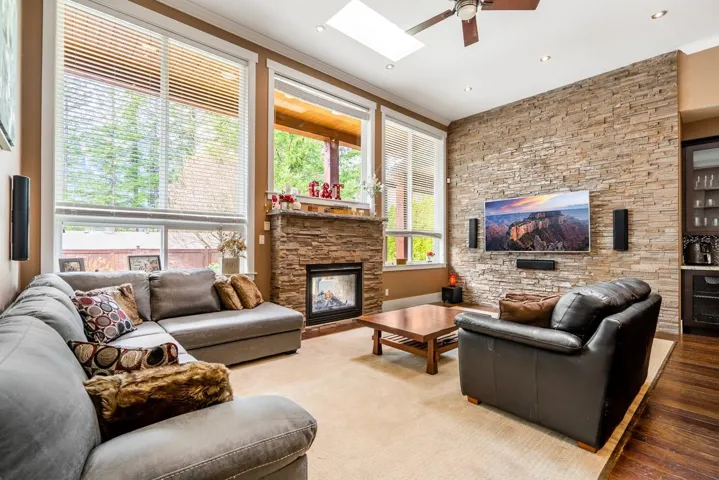 Living area featuring a stone fireplace, a skylight, ceiling fan, and ornamental molding