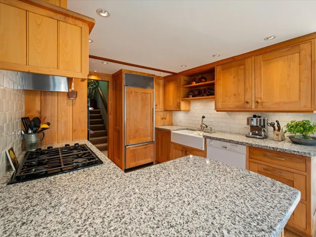 Kitchen featuring decorative backsplash, brown cabinetry, black gas cooktop, open shelves, and light stone counters