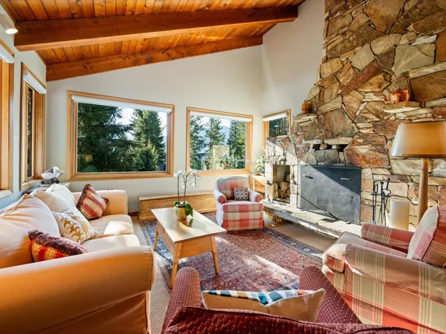 Living room with a wood ceiling with exposed beams, a stone fireplace, and high vaulted ceiling
