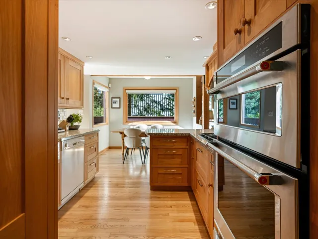 Kitchen featuring appliances with stainless steel finishes, brown cabinets, light wood-type flooring, light stone countertops, and recessed lighting