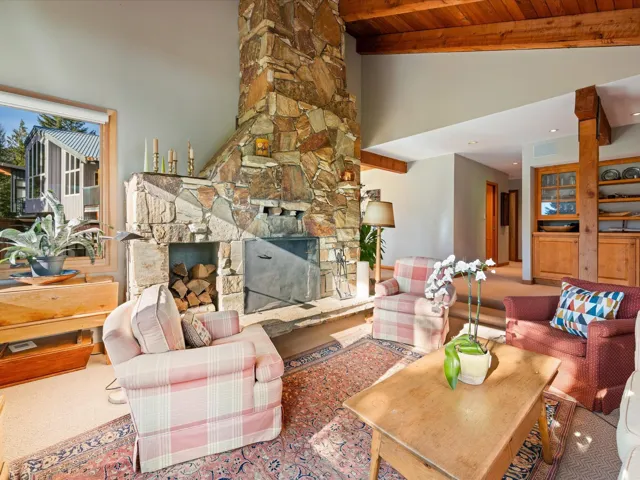 Carpeted living area featuring a stone fireplace, high vaulted ceiling, and a wooden ceiling with exposed beams