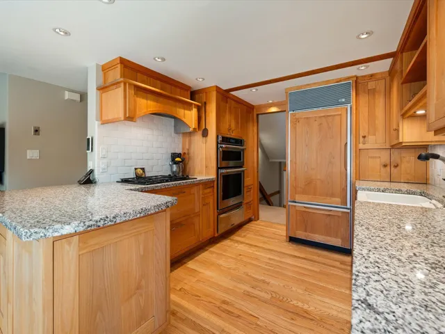 Kitchen featuring tasteful backsplash, light stone counters, light wood-style floors, paneled refrigerator, and recessed lighting