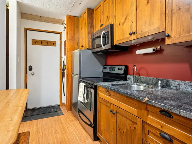 Kitchen featuring electric stove, brown cabinetry, light wood-type flooring, a textured ceiling, and dark stone countertops