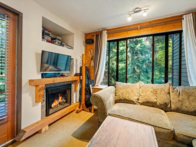 Carpeted living area featuring a textured ceiling, a glass covered fireplace, and view of wooded area