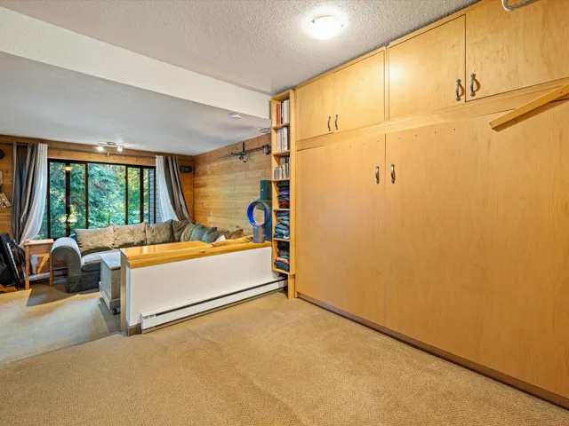 Bedroom featuring wooden walls, a baseboard heating unit, light carpet, and a textured ceiling