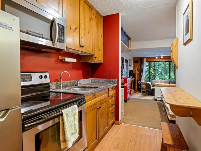 Kitchen with appliances with stainless steel finishes, brown cabinetry, light wood finished floors, a textured ceiling, and light colored carpet