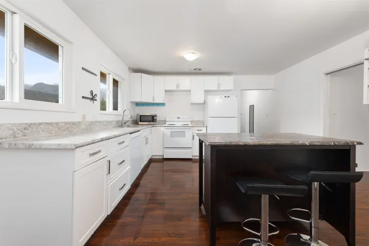 Kitchen with white appliances, white cabinets, dark wood finished floors, a center island, and a sink