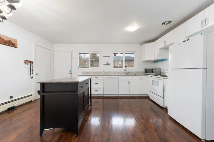 Kitchen featuring white appliances, dark wood-style flooring, a sink, white cabinets, and light stone countertops