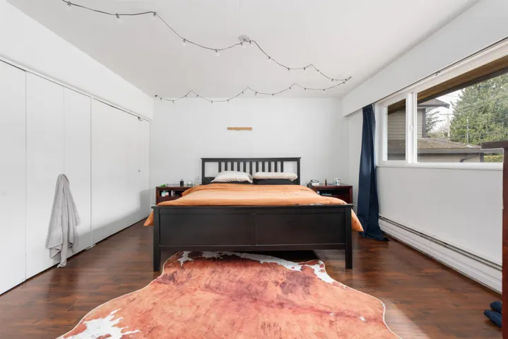 Bedroom with a baseboard heating unit, dark wood-style flooring, and a closet