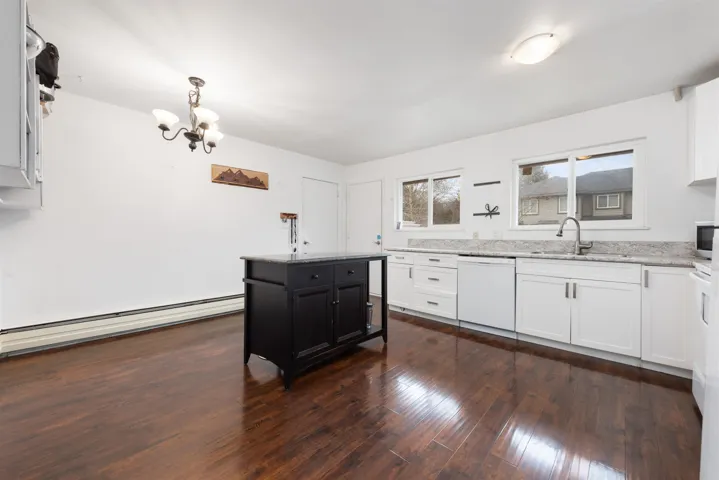 Kitchen featuring dark wood-type flooring, light stone countertops, white dishwasher, dark cabinetry, and a sink