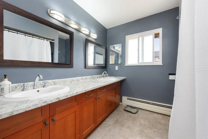 Full bath featuring double vanity, a baseboard radiator, a sink, and tile patterned flooring