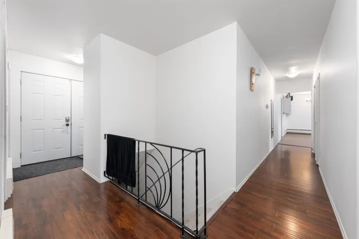 Hallway with hardwood / wood-style flooring, baseboard heating, an upstairs landing, and baseboards