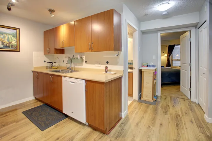 Kitchen featuring light countertops, white dishwasher, brown cabinetry, light wood-type flooring, and a textured ceiling