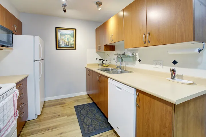 Kitchen featuring brown cabinetry, decorative backsplash, white appliances, light countertops, and light wood finished floors