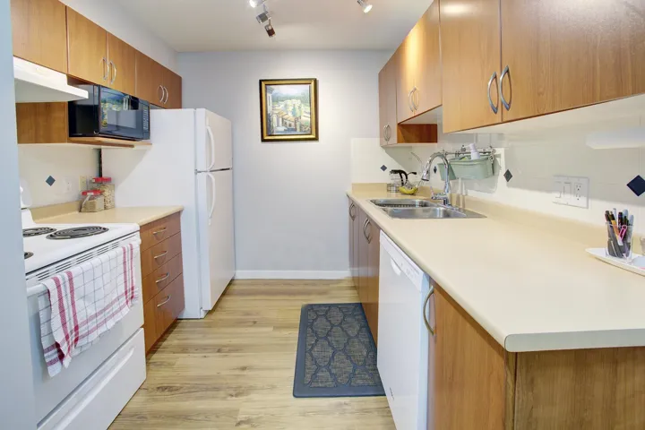 Kitchen with white appliances, brown cabinets, light wood-style flooring, light countertops, and under cabinet range hood