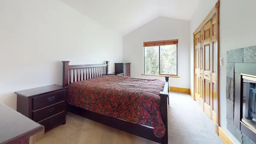 Bedroom featuring vaulted ceiling, light colored carpet, a closet, and a tile fireplace