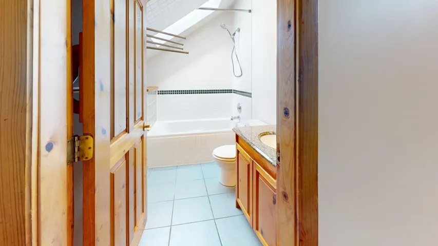 Bathroom featuring a skylight, tiled shower / bath, vanity, and light tile patterned floors
