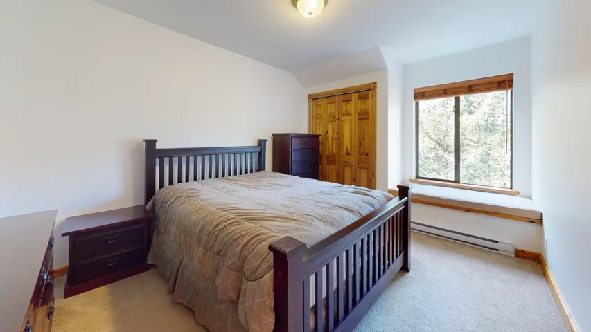 Bedroom featuring baseboard heating, light carpet, a closet, and lofted ceiling