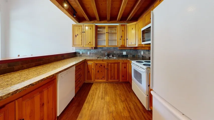 Kitchen featuring white appliances, glass insert cabinets, light wood-style floors, backsplash, and brown cabinetry