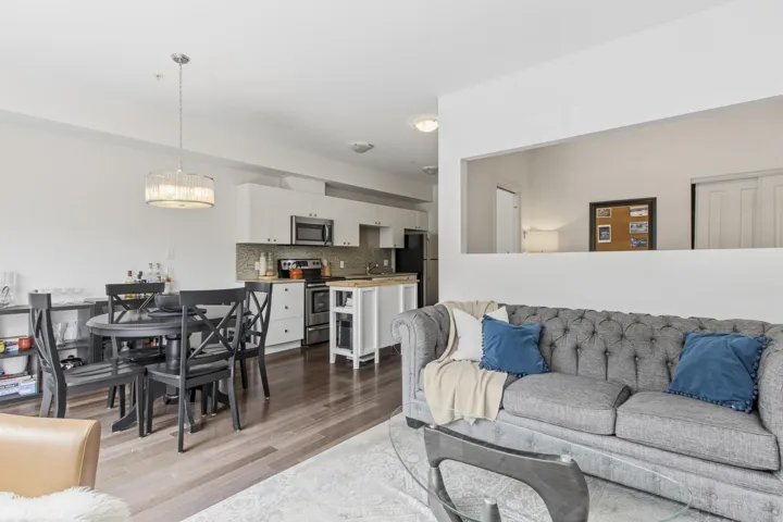 Open-concept living space featuring wood-finish flooring, a contemporary kitchen with white cabinetry and stainless steel appliances, a kitchen island with a wood countertop, and a dining area illuminated by a modern pendant light fixture