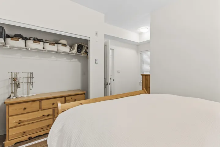 Bedroom space featuring a built-in closet with wire shelving, smooth white walls, and wood-finish flooring