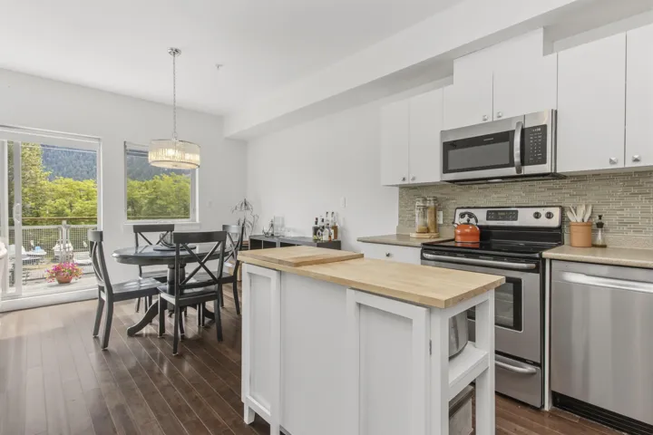 Open-concept kitchen and dining area featuring rich wood-finish flooring, white cabinetry, stainless steel appliances, and a mosaic tile backsplash