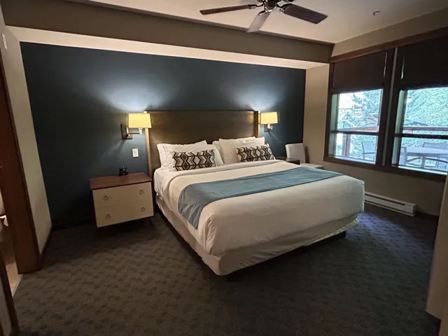 Spacious room featuring a dark accent wall, wood-finish headboard, wall-mounted sconce lighting, and a ceiling fan