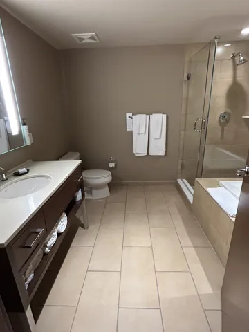 Spacious bathroom featuring a dark wood-finish vanity with an integrated white sink, a glass-enclosed shower with a built-in tub, and large format tile flooring