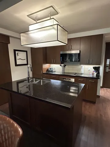 Kitchen featuring dark wood-finish cabinetry, a black speckled countertop, and a stainless steel microwave