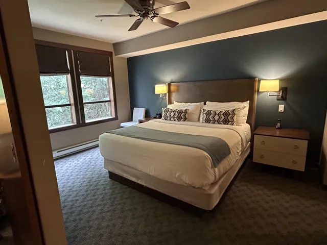 Spacious bedroom featuring a wood-finish headboard, twin wall-mounted sconces, and a ceiling fan with integrated lighting
