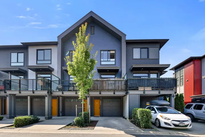 Contemporary townhome exterior with mixed siding, private balconies featuring glass and metal railings, and integrated single-car garages