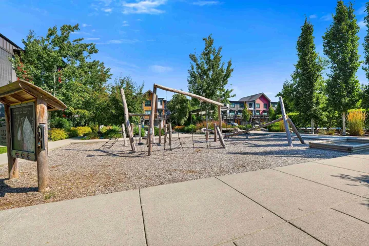Community playground featuring natural wood play structures, rope climbing elements, and a sand area