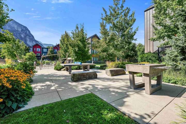 Concrete patio area with built-in game tables, surrounding green spaces, and mature trees